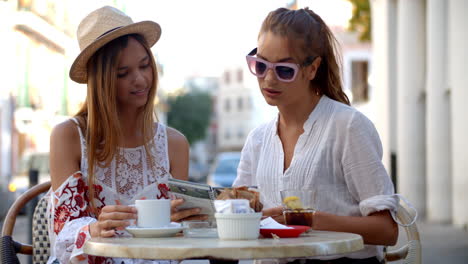 Zwei-Freundinnen-Lesen-Einen-Reiseführer-Vor-Einem-Café,-Ibiza